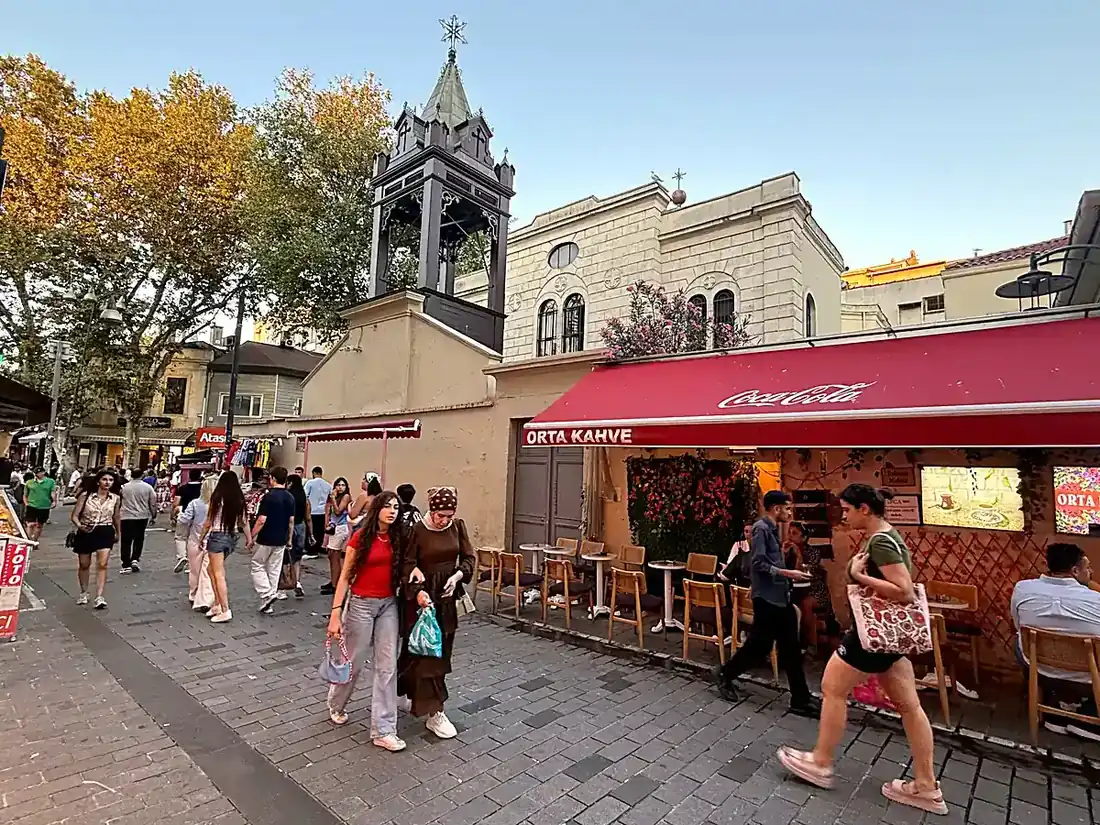 People strolling past a pavement café by the Surp Takavor church as dusk settles over Kadıköy, Istanbul