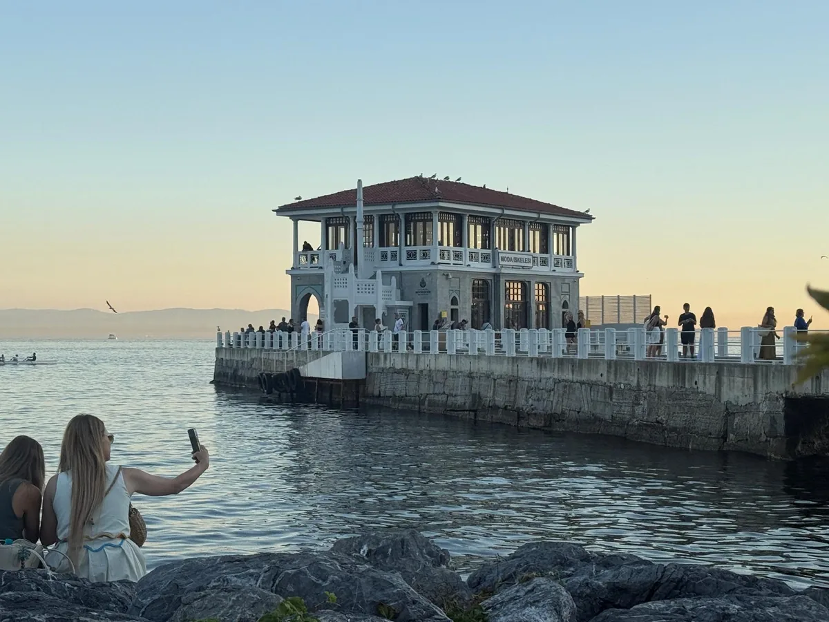 People watching the October sunset from the rocks by Moda Pier, Kadıköy, one photographing the historic ferry terminal