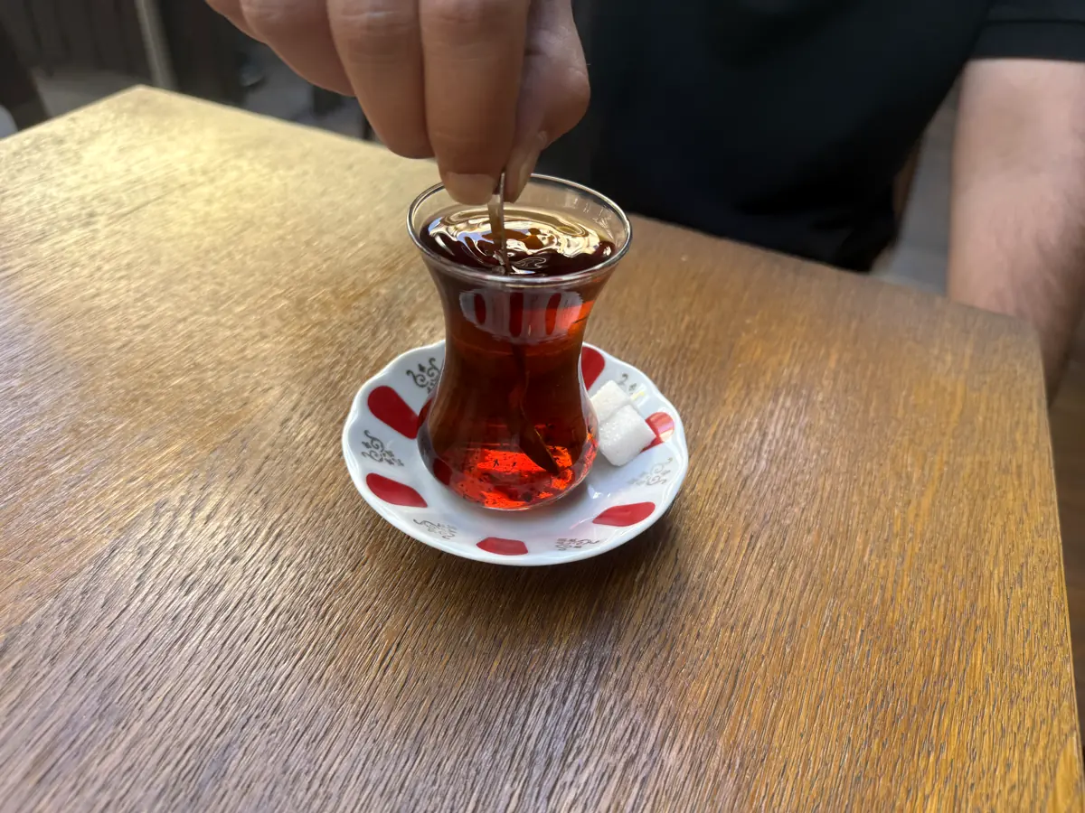 Stirring a tulip-shaped glass of Turkish tea on a wooden café table in Kadıköy, Istanbul — the most common of all Turkish drinks