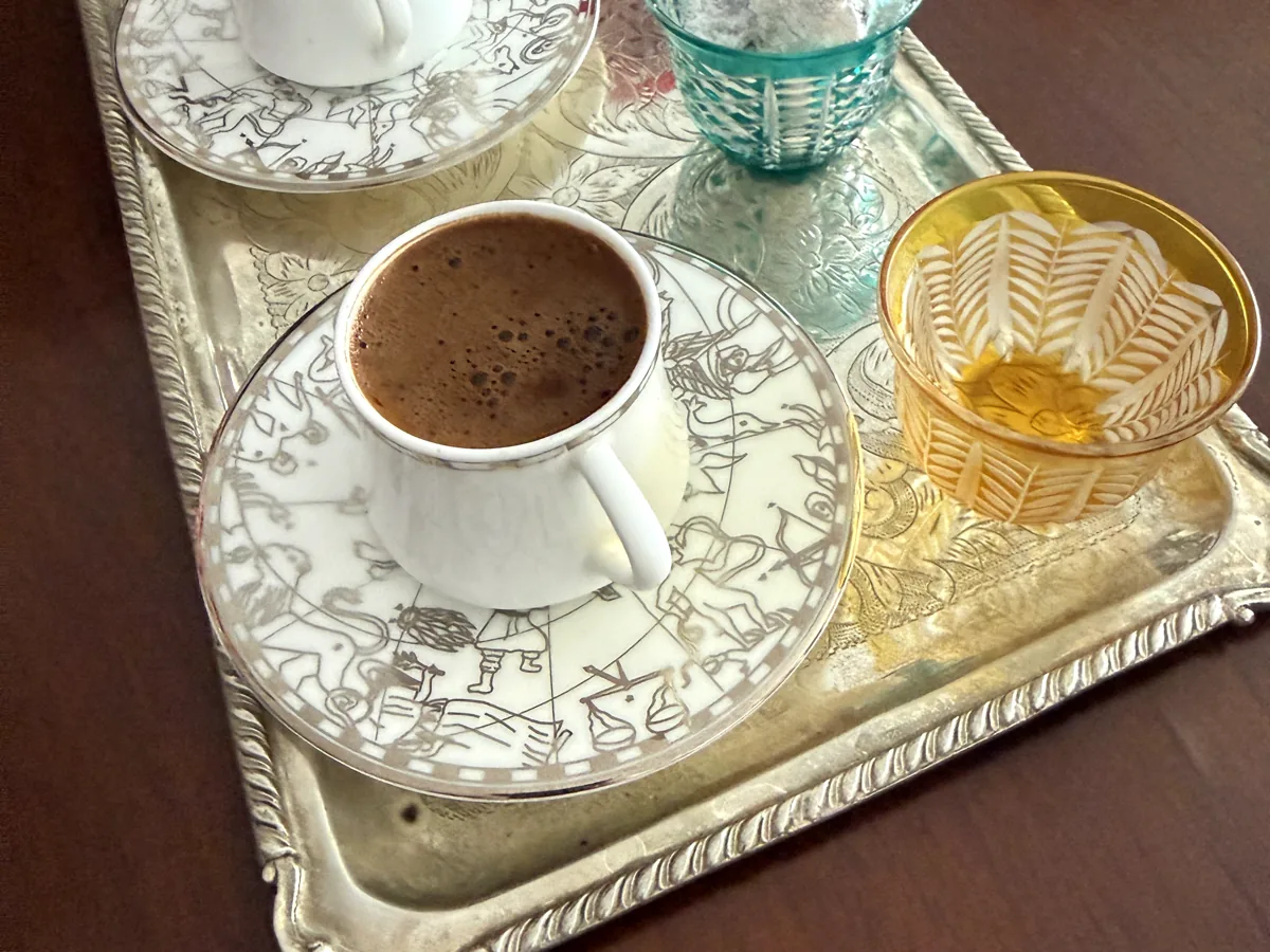 A cup of foamy Turkish coffee on an engraved silver tray with a small dish of Turkish delight, served in Kadıköy