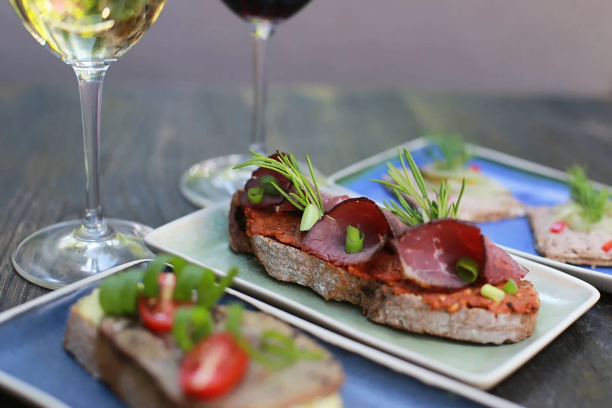 Turkish meze plates — pastırma on sourdough and vegetable small plates — beside glasses of white and red Turkish wine at WAYANA Wine Bar in Moda, Kadıköy